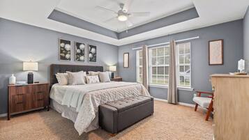 Une chambre à coucher comprenant un lit, des tables de chevet, un banc, une commode et un ventilateur de plafond.