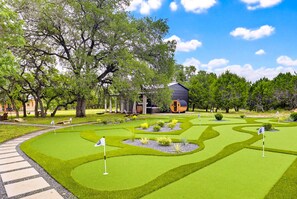 A miniature golf course with a winding path, flag holes, and a building in the background. - Stillstone Ranch | A Wellness Retreat | Sleeps 32 (Driftwood)