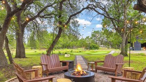 An outdoor seating area with Adirondack chairs, a fire pit, and string lights.