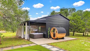 A modern outdoor sauna with a hot tub, a wooden barrel sauna, and a covered seating area.