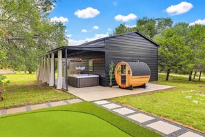 Uma sauna moderna ao ar livre com hidromassagem, uma sauna em formato de barril de madeira e uma área de estar coberta.