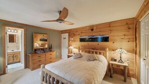 A wooden-paneled bedroom with a bed, bedside tables, a ceiling fan, a mirror, and a painting. - Lower Darby by Avantstay Indoor Heated Pool + Billiards + Foosball Near Gore (North Creek)