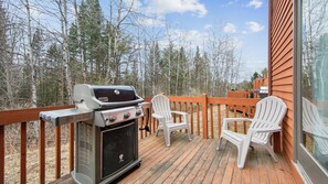 A deck with a Weber Spirit grill, white Adirondack chairs, and a wooden railing overlooking a forest. - Lower Darby by Avantstay Indoor Heated Pool + Billiards + Foosball Near Gore (North Creek)