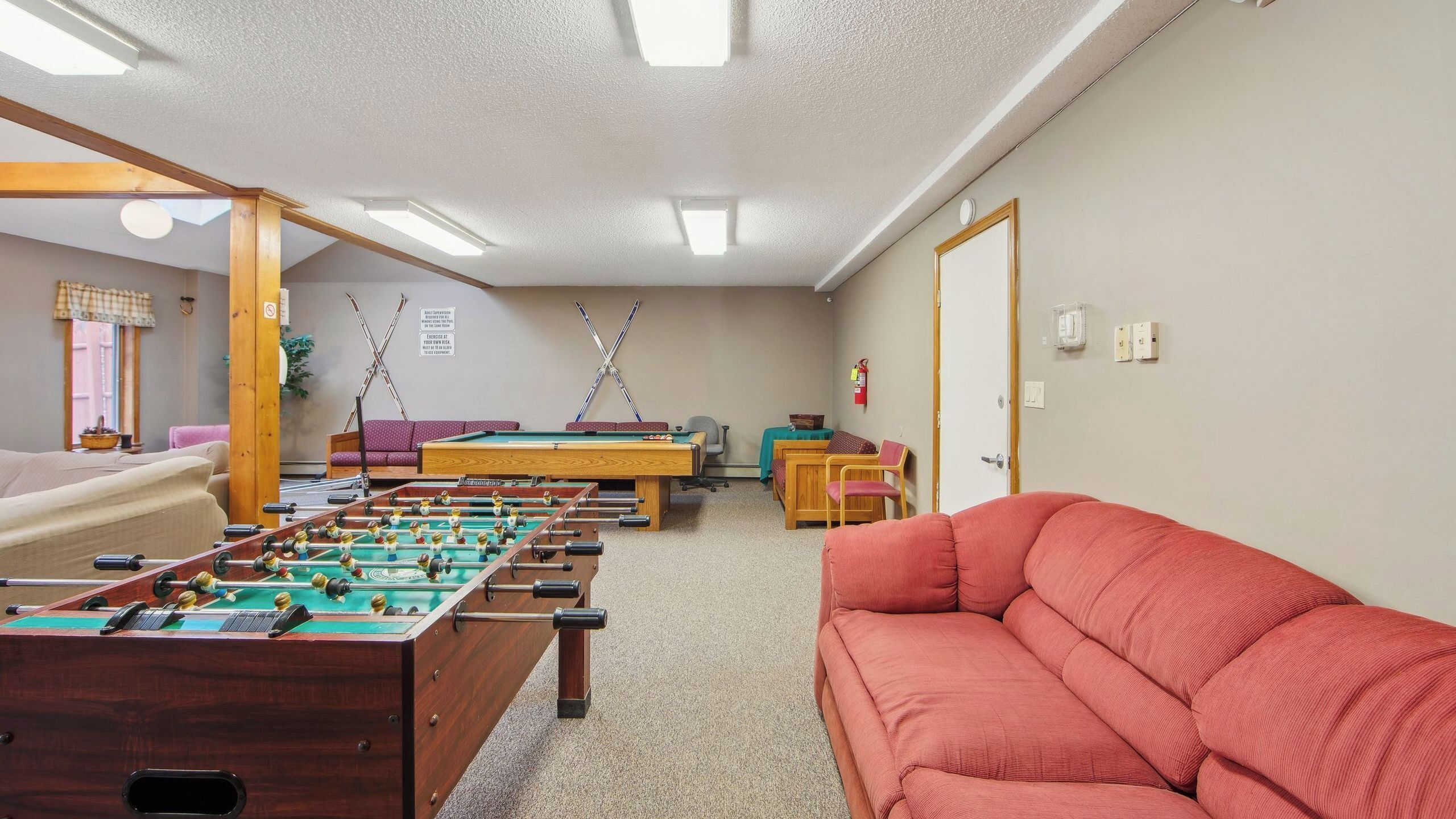 A room with a foosball table, pool table, and a red sofa.