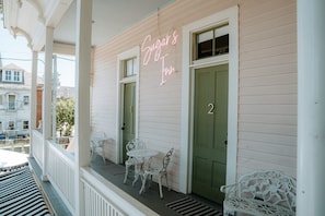 Ein Gebäude mit einem Neonlichtschild, das 'Sugar's Inn' zeigt, einer grünen Tür und weißen Gartenmöbeln auf der Veranda.