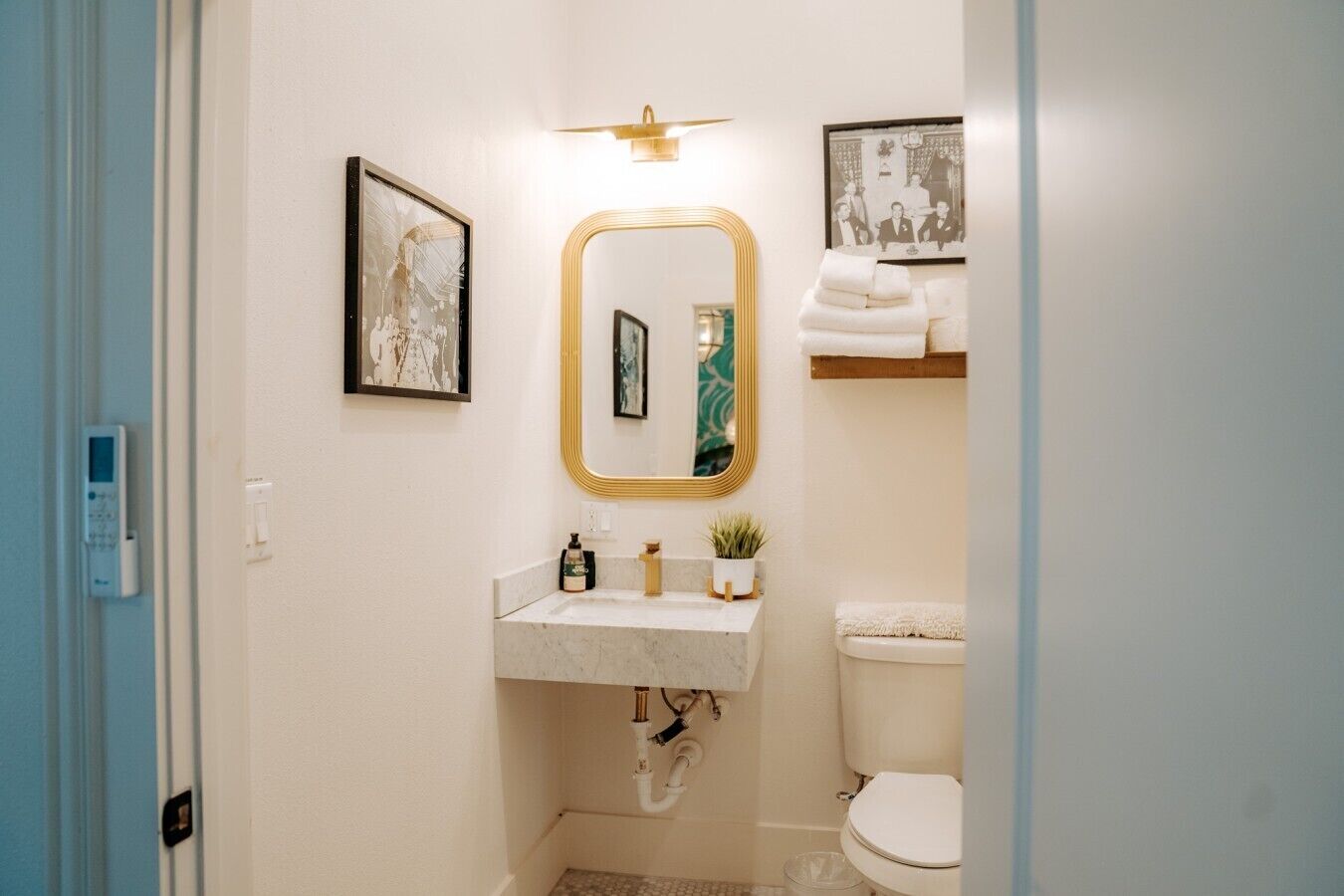 Une salle de bain avec un lavabo en marbre, un miroir encadré d’or, des toilettes et une petite étagère avec des serviettes.