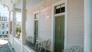 Ein Gebäude mit einem Neonlichtschild, das 'Sugar's Inn' zeigt, einer grünen Tür und weißen Gartenmöbeln auf der Veranda.