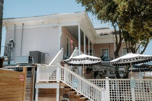 A building with a porch, outdoor seating with umbrellas, and a staircase leading to the entrance. - Sugars INN Room #2 in Galveston (Galveston)
