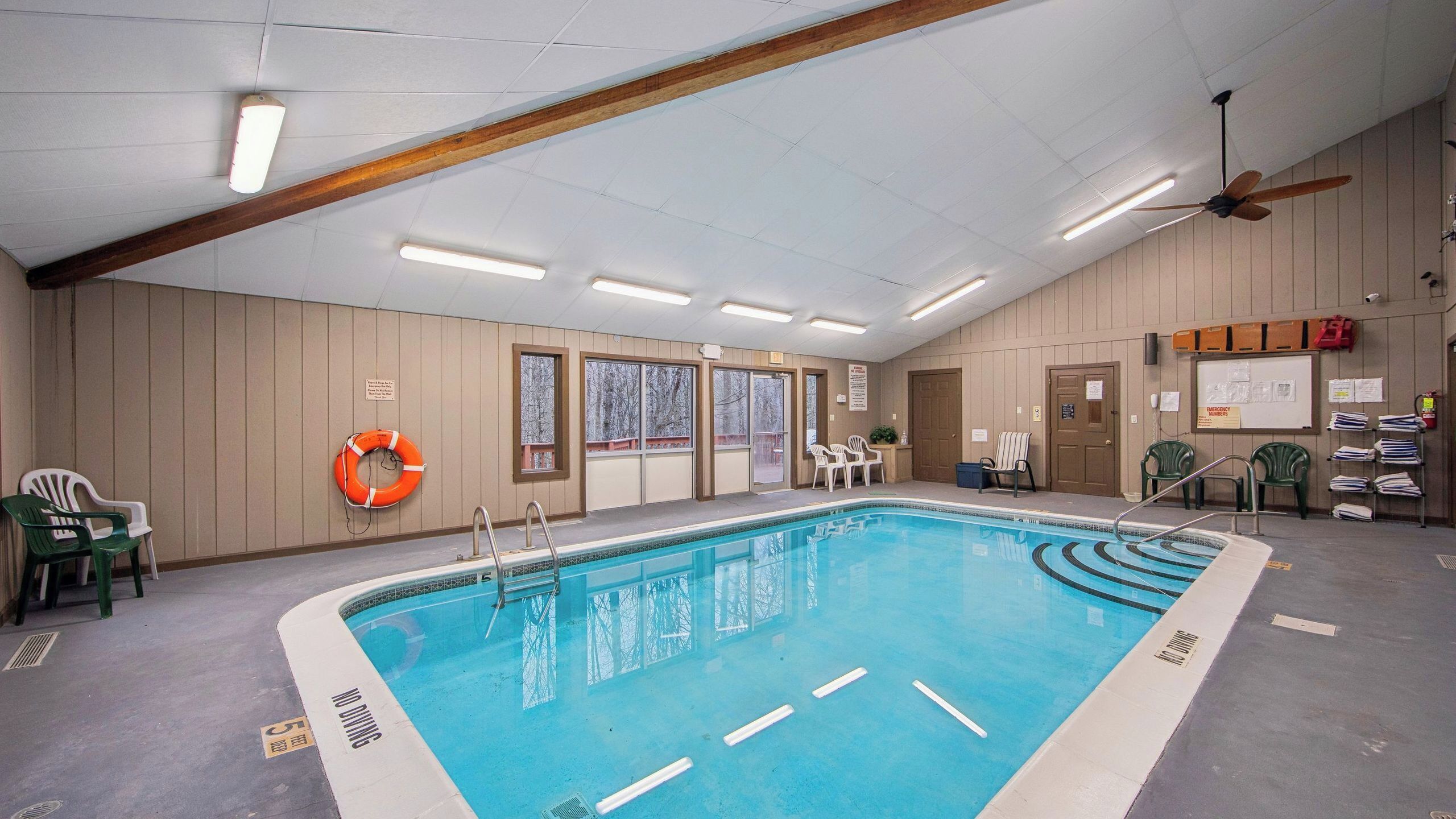 An indoor swimming pool with clear lane markings, a lifebuoy, and a ceiling fan.