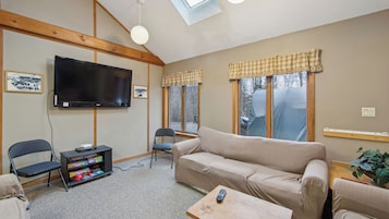 A living room with a TV, sofa, chairs, and a bookshelf.