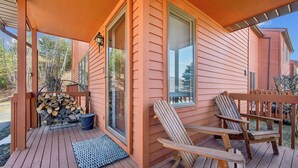 A wooden deck with two Adirondack chairs, a fire pit, and a stack of firewood.