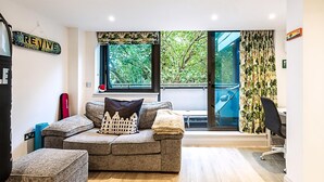 Ein modernes Wohnzimmer mit einem grauen Ecksofa, einem kleinen Hocker, einer roten Yogamatte und einem Schreibtisch mit Stuhl.