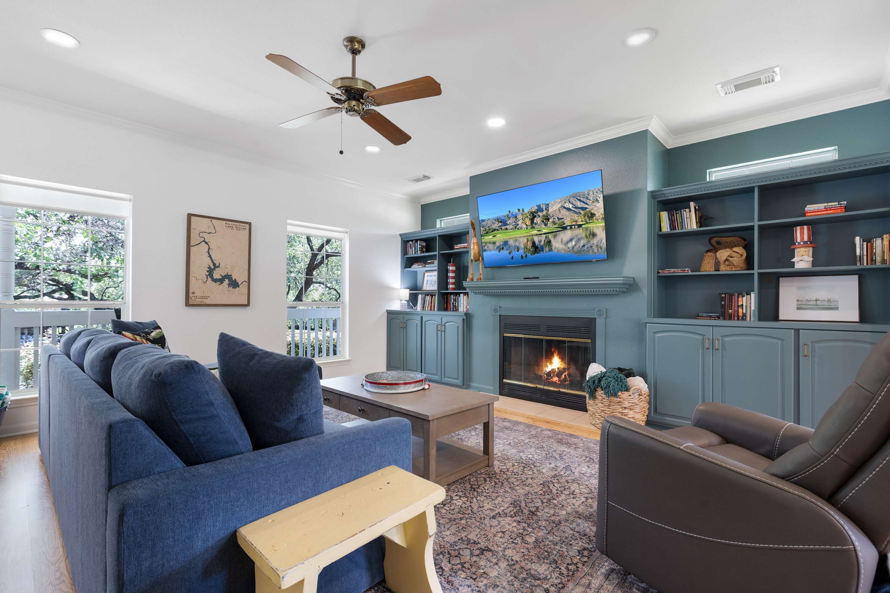 A living room with a sofa, armchair, TV, fireplace, bookshelves, and a ceiling fan.