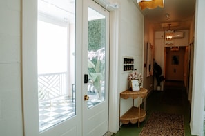 Ein Flur mit Glastür zum Balkon, ein kleiner Tisch mit Blumenvase und ein Wandregal mit Dekoration.