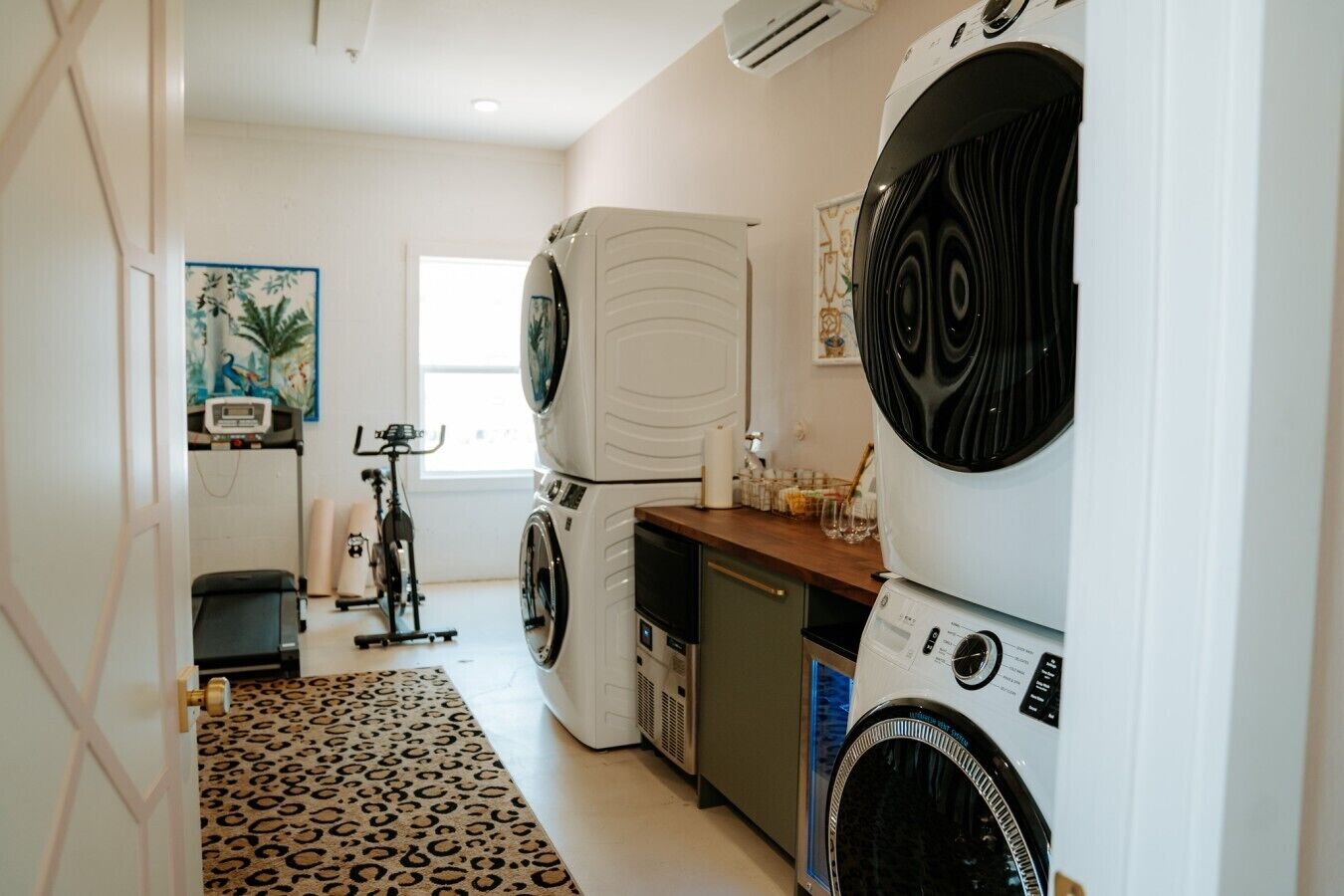 A laundry room with two stacked washing machines, a small refrigerator, and a treadmill.