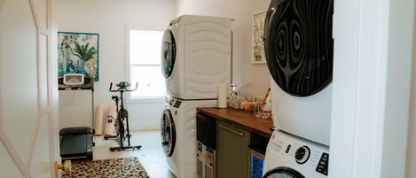 A laundry room with two stacked washing machines, a small refrigerator, and a treadmill.