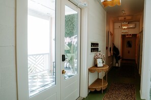 Un corridoio con una porta in vetro che dà su un balcone, un tavolino con un vaso di fiori e una mensola a parete con oggetti decorativi.