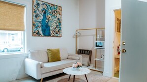 Una sala de estar con sofá, mesa de centro, cuadro, radiador, microondas y puerta.