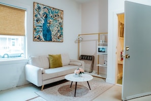 Ein Wohnzimmer mit einer Couch, einem Couchtisch, einem Gemälde, einer Heizung, einer Mikrowelle und einer Tür.