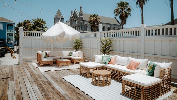 A wooden deck with wicker furniture, including a sofa and chairs, under a white umbrella. - Room #10 The Oleander Hotel Galveston (Galveston)