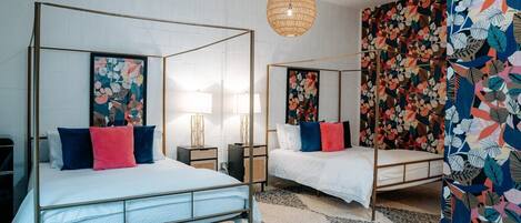 Una habitación con dos camas con dosel, una lámpara colgante y un papel tapiz estampado con motivos florales.