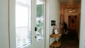 A hallway with a glass door leading to a balcony, a small table with a vase of flowers, and a wall-mounted shelf with decorative items. - Room #10 The Oleander Hotel Galveston (Galveston)