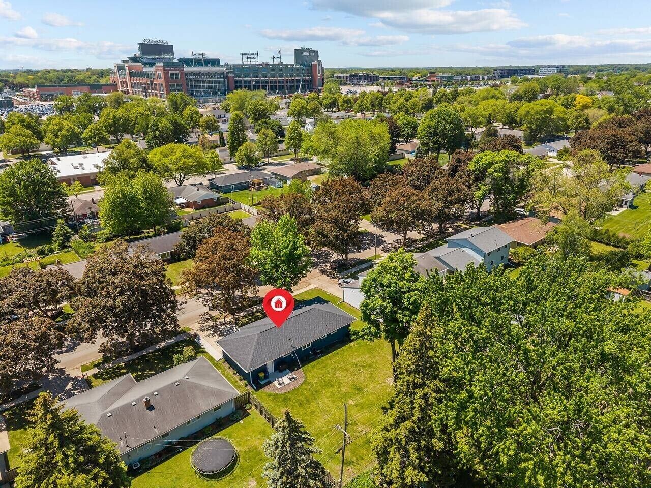 Vista aérea de una zona residencial con casas, árboles y un edificio grande al fondo.