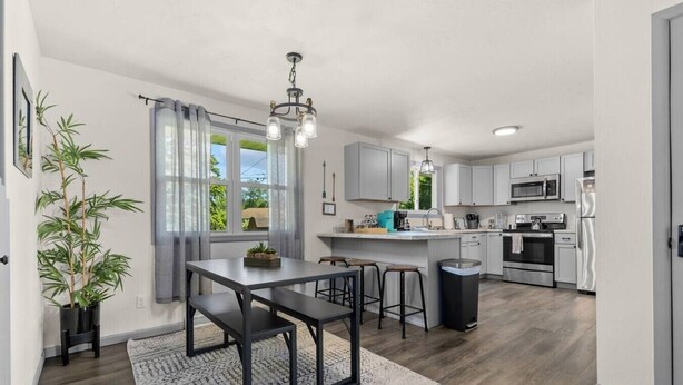 A modern kitchen with a dining area, wooden flooring, and a large window with curtains.