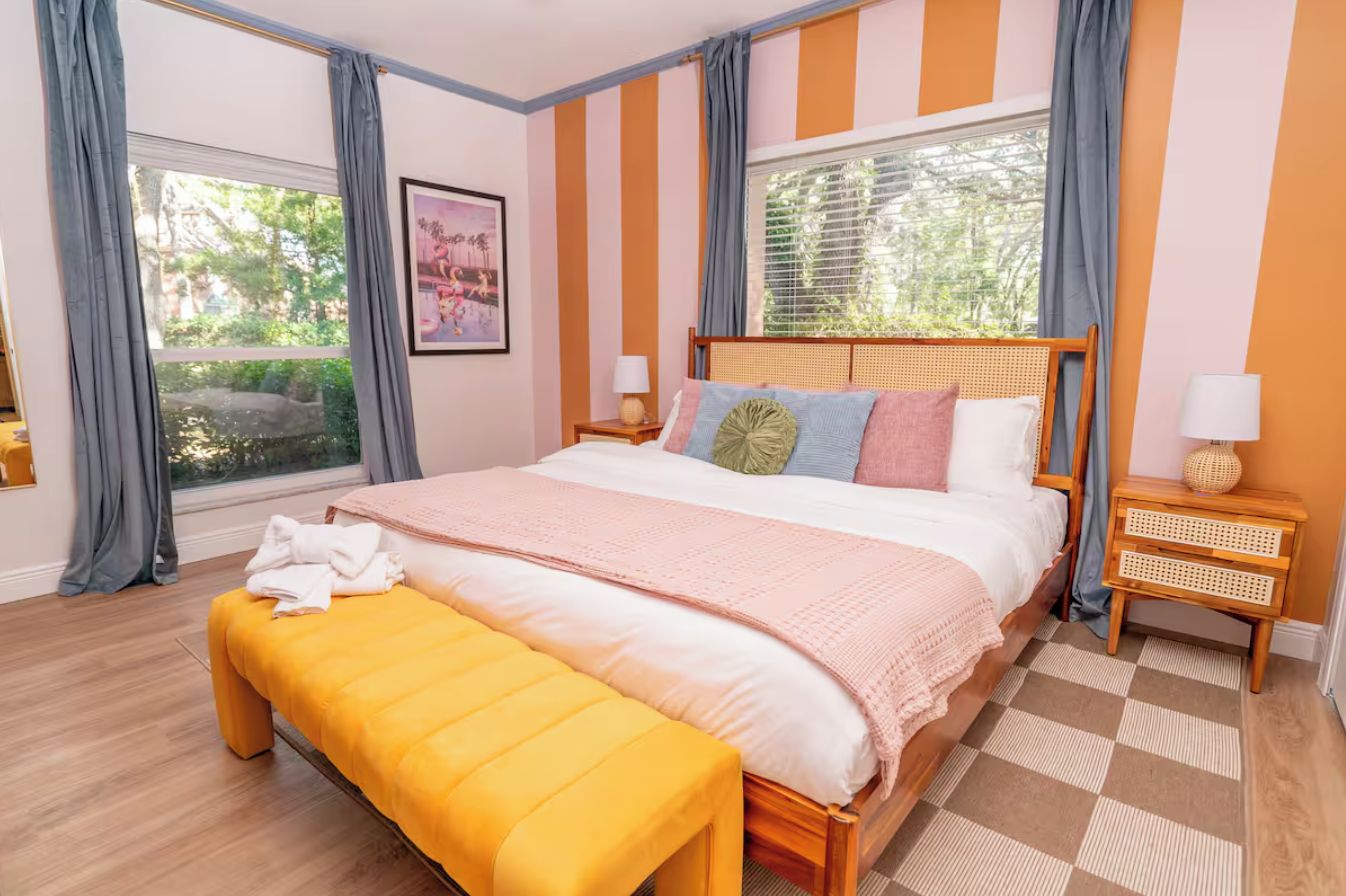 Een slaapkamer met een groot bed, een bankje, een nachtkastje en een raam met gordijnen.