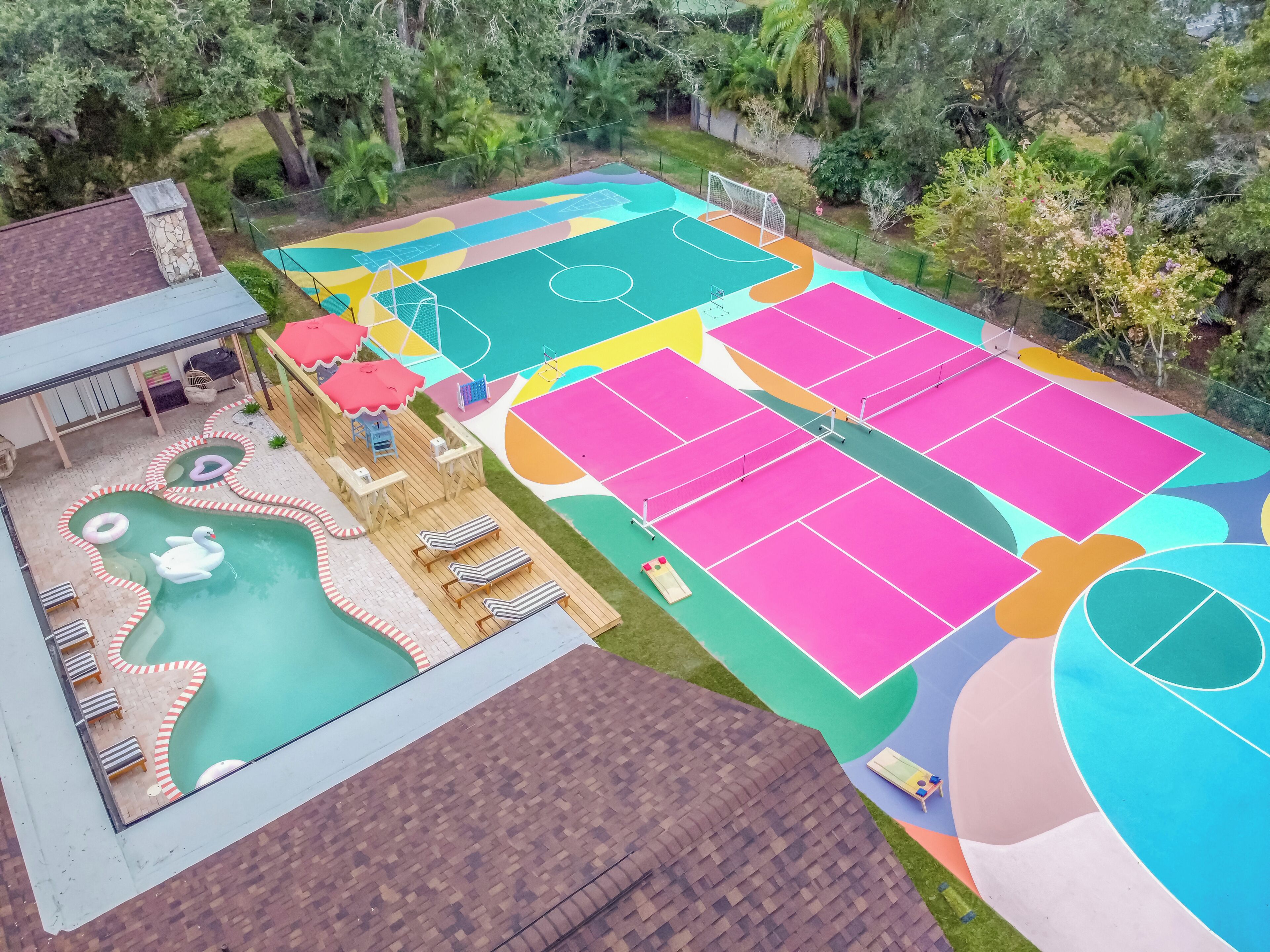 A multi-purpose outdoor area with a swimming pool, sun loungers, a small wooden deck, and a colorful sports court.