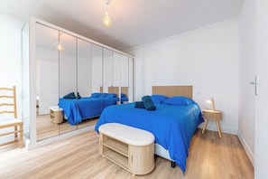 Ein Schlafzimmer mit einem großen Spiegel, einem Bett mit blauer Bettwäsche, einer hölzernen Bank und einem Nachttisch mit einer Lampe.