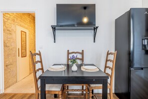 Ein Essbereich mit einem dunklen Holztisch, vier Holzstühlen, einer kleinen weißen Vase mit Blumen und einem schwarzen, an der Wand befestigten Regal über dem Tisch.