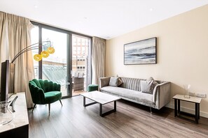 A modern living room with a sofa, a green armchair, a coffee table, a floor lamp, and a painting on the wall. - Aldgate East Apartment With Balcony (London)
