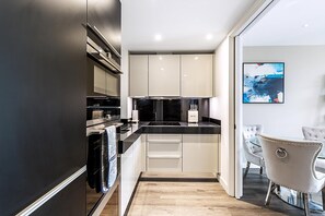 A modern kitchen with a black countertop, white cabinets, and a dining area with a white table and chairs. - Aldgate East Apartment With Balcony (London)