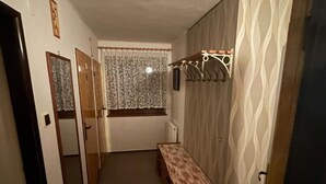 Um corredor estreito com um banco, um porta-roupas e uma janela com cortinas estampadas.