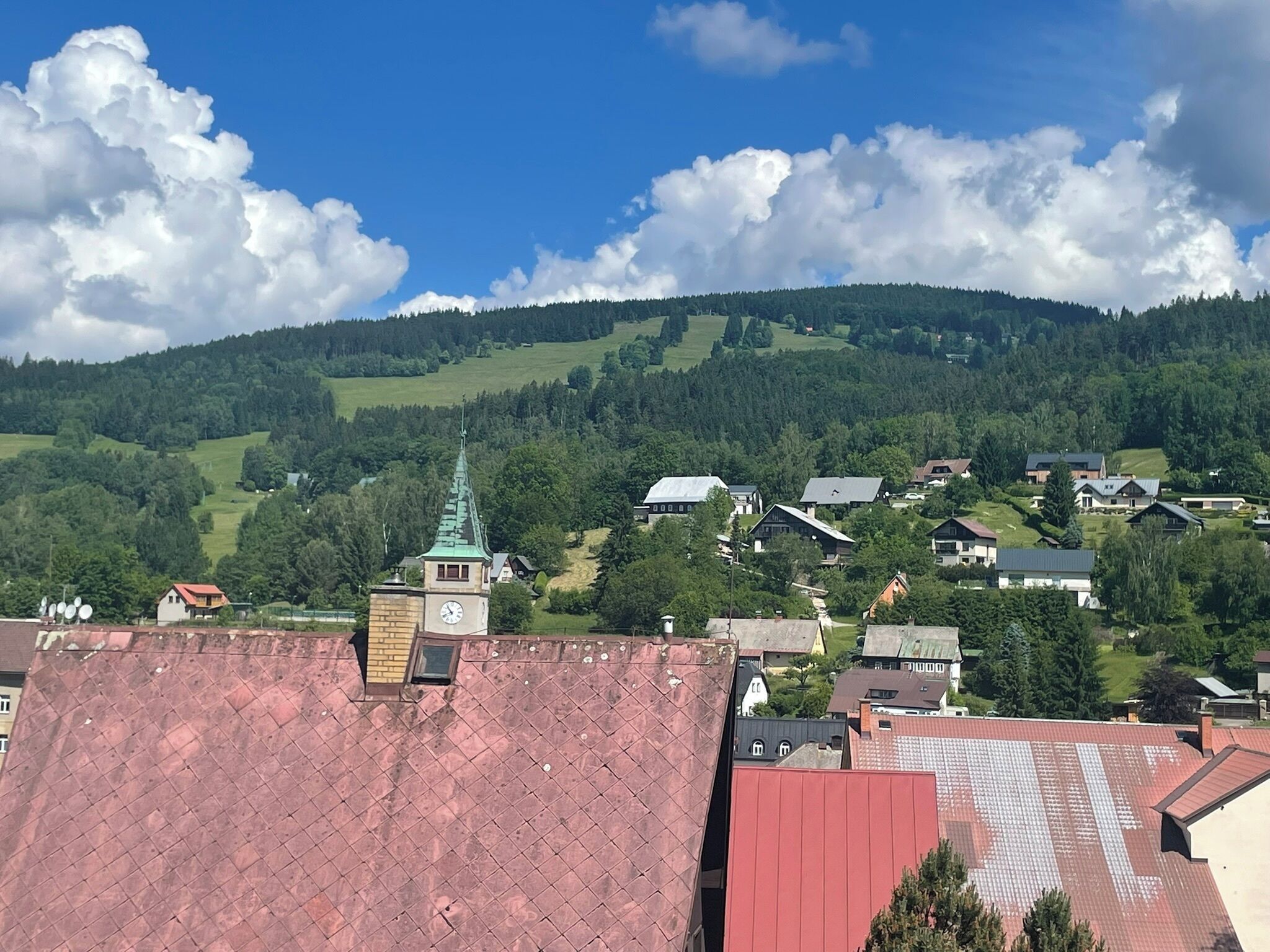 A town with a prominent church tower, surrounded by residential buildings and green hills.