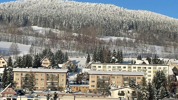 Montanha coberta de neve com área residencial em primeiro plano, incluindo edifícios altos com sacadas.