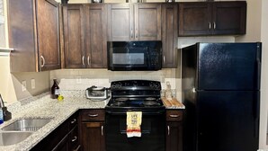 Uma cozinha com armários de madeira escura, um micro-ondas preto, um fogão preto e uma geladeira preta.