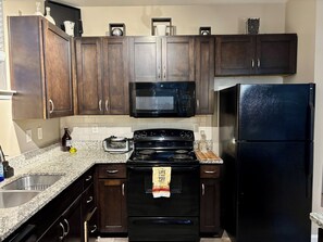 Une cuisine avec des meubles de rangement en bois foncé, un micro-ondes noir, une cuisinière noire et un réfrigérateur noir.