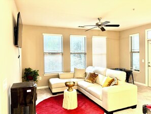 Ein Wohnzimmer mit Ecksofa, Deckenventilator und Wandfernseher.
