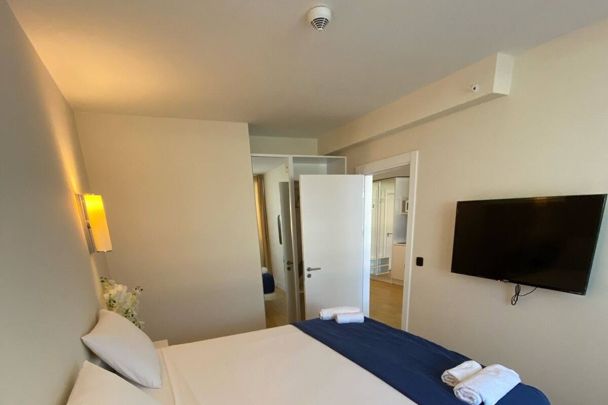 Habitación de hotel con una cama, televisión, lámpara de noche y puerta que da a un baño.