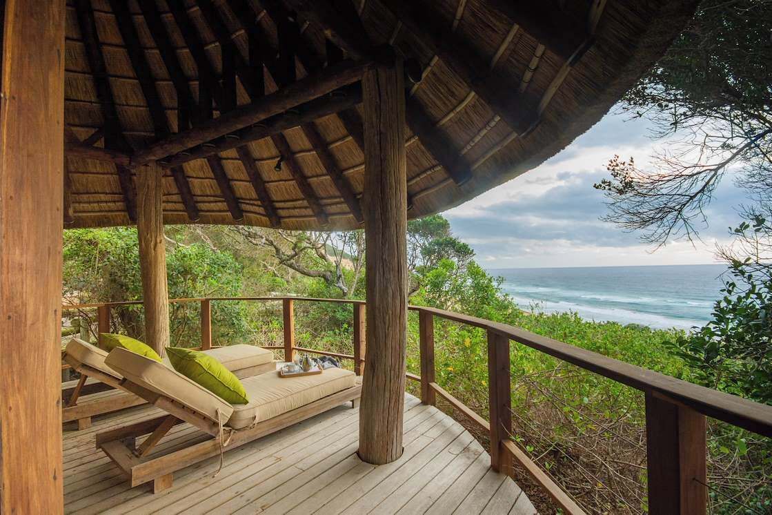 A wooden deck with lounge chairs and a thatched roof structure overlooking the ocean.