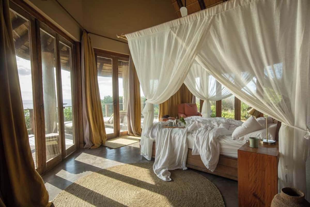 A bedroom with a canopy bed, large windows, and a view of the outdoors.