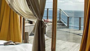 Una habitación con cama, ventana con cortinas y vista a un balcón y al océano.