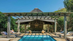 Una piscina con sillas de descanso y una estructura de techo de paja.