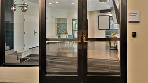 Ein moderner Arbeitsraum mit Glastür zu einem Loungebereich, einem Konferenzraum mit großem Gemälde und einer sichtbaren Treppe.