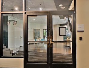 Ein moderner Arbeitsraum mit Glastür zu einem Loungebereich, einem Konferenzraum mit großem Gemälde und einer sichtbaren Treppe.