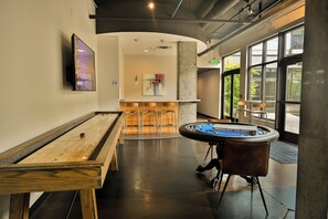 Ein Billardtisch, ein Kicker und eine Bar mit Hockern in einem modernen Innenbereich mit großen Fenstern.