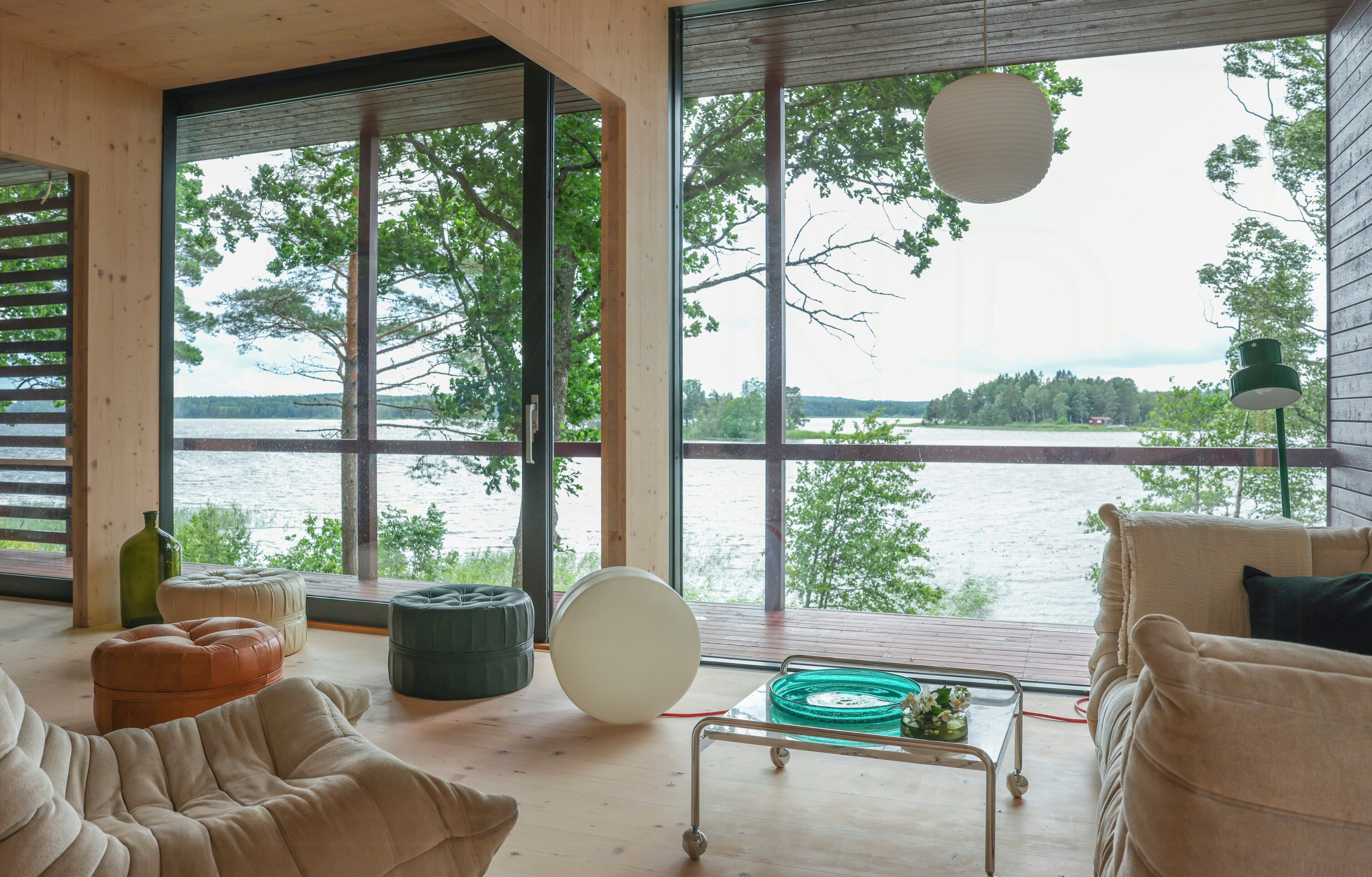 En modern inredning med stora fönster, ett trägolv och utsikt över en sjö.