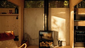 A cozy cabin interior with a wood-burning stove, a sofa, a chair, and a dining area. - Architect-designed cabin with Harefjord views (Säffle)